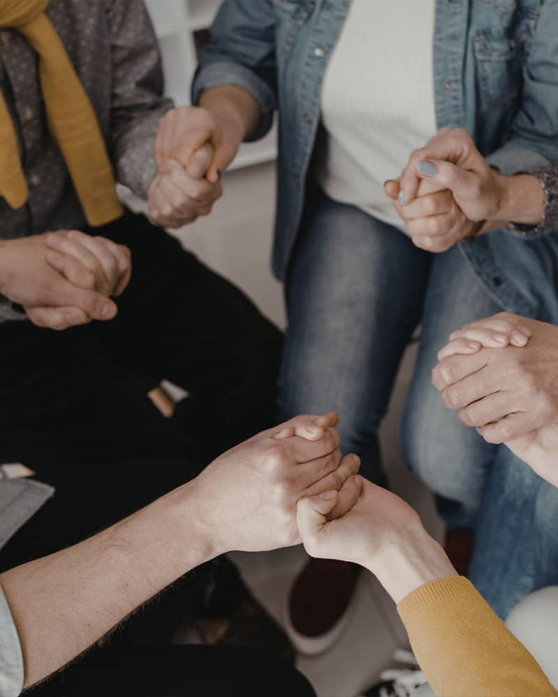 a circle of four people hold each others hands, close up on their hands
